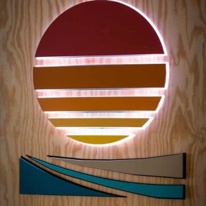 Multi colored wooden slats in the shape of a sun with light shining from behind.